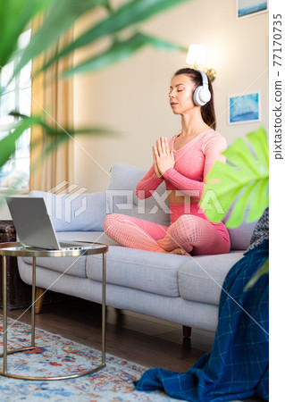 Woman exercising at home. She stretches the muscles of the legs and back with a tutorial from the Internet. Vertical photo. 77170735