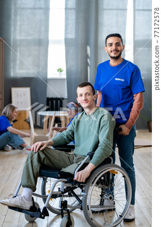 Young male volunteer standing next to guy in a wheelchair 77172578