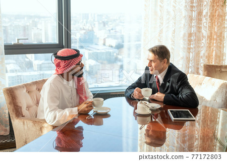 Intercultural delegates sitting at a table and holding coffee cups 77172803