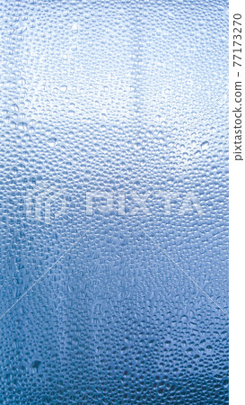 Raindrops on the glass in rainy weather.The glittering, shiny surface of water on glass.Water drops in the form of balls or spheres.Blue raindrops background. Abstract backgrounds ornament with water 77173270