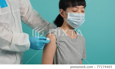 Vaccine Concept. Woman waiting for coronavirus vaccine injection by doctor. Asian woman with medical mask open shoulder and upper arm on blue green background. Waiting for vaccination. 77174405