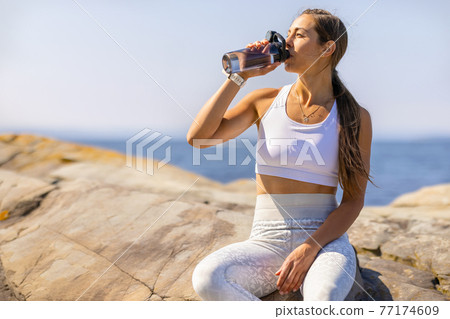 Female Athlete Drinking Water During Outdoor Workout by the Sea 77174609