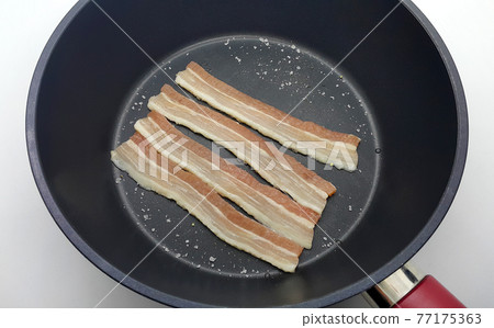 Raw bacon in a frying pan for making breakfast 77175363