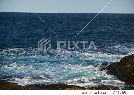 Small sea waves break against the stones of the shore. A bright sunny day and white foam of the waves. Melting glaciers as an environmental impact of air pollution. Small sea waves break against the stones of the shore. A bright sunny day and white foam of the waves. Melting glaciers as an environmental impact of air pollution. 77176994