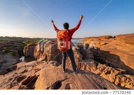 Back of tourist man, a backpacker people, travel in Sam Phan Bok, Ubon Ratchathani, Thailand. Dry rock with mountain hills. Nature landscape. Grand Canyon of Thailand. Adventure lifestyle activity. Back of tourist man, a backpacker people, travel in Sam Phan Bok, Ubon Ratchathani, Thailand. Dry rock with mountain hills. Nature landscape. Grand Canyon of Thailand. Adventure lifestyle activity. 77178146