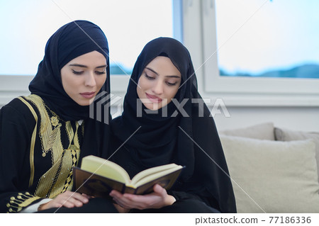 Portrait of young muslim women reading Quran in modern home. Portrait of young muslim women reading Quran in modern home. 77186336