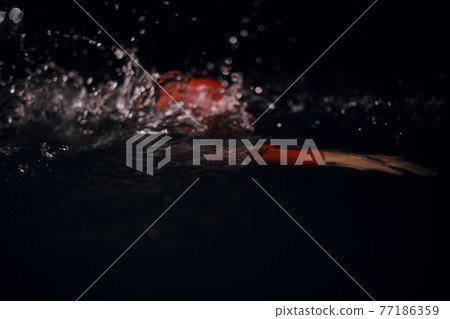 triathlon athlete swimming in dark night wearing wetsuit 77186359