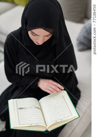 Portrait of young muslim woman reading Quran in modern home 77186450