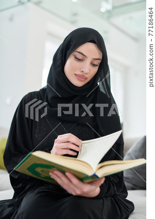 Portrait of young muslim woman reading Quran in modern home Portrait of young muslim woman reading Quran in modern home 77186464