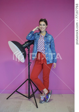 Young woman leaning against studio flashlight over a pink background 77187768
