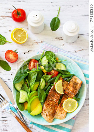 Grilled salmon fillet close-up with spinach, cucumber, tomato and avocado salad on a white wooden table. 77188550