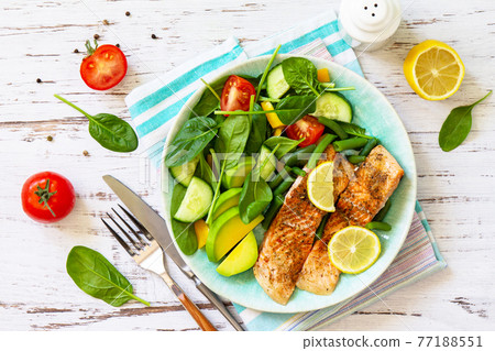 Grilled salmon fillet close-up with spinach, cucumber, tomato and avocado salad on a white wooden table. Top view, flat lay. Grilled salmon fillet close-up with spinach, cucumber, tomato and avocado salad on a white wooden table. Top view, flat lay. 77188551