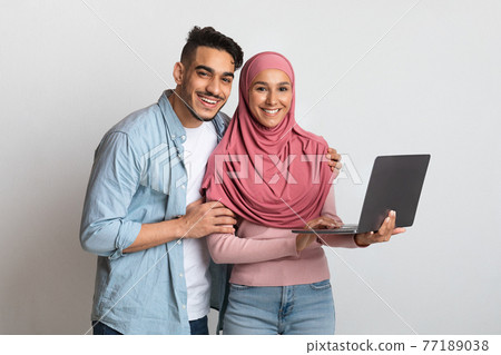 Portrait Of Happy Islamic Couple Posing With Laptop Computer In Hands 77189038