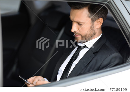 Wealthy manager sitting in car and using smartphone 77189199