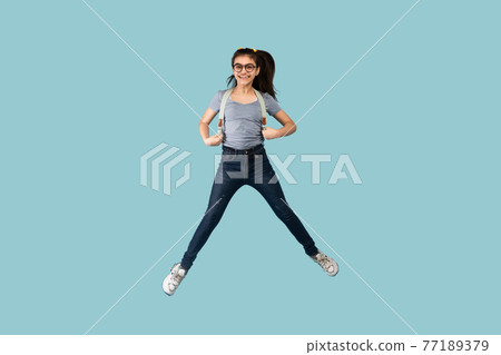 Excited Indian teen schoolgirl with backpack jumping up in air on blue studio background Excited Indian teen schoolgirl with backpack jumping up in air on blue studio background 77189379