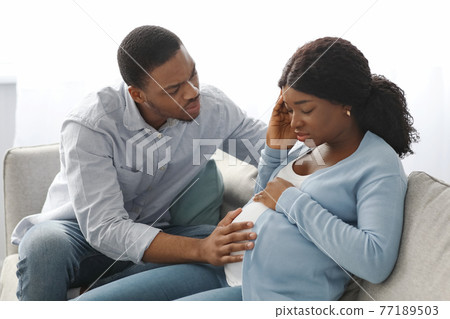 Black pregnant lady feeling sick, worried husband sitting by her Black pregnant lady feeling sick, worried husband sitting by her 77189503