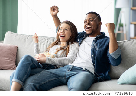 Home Entertainment. Happy Interracial Couple Watching Tv And Cheering Sports At Home Home Entertainment. Happy Interracial Couple Watching Tv And Cheering Sports At Home 77189616