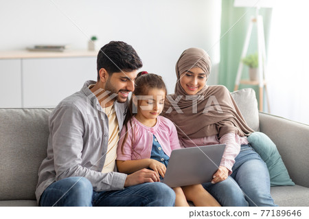 Young muslim parents and girl using laptop together, surfing internet or having video chat with someone, sittig on sofa Young muslim parents and girl using laptop together, surfing internet or having video chat with someone, sittig on sofa 77189646