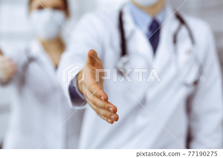Unknown man-doctor and woman standing straight as a team and offering helping hand in modern clinic. Perfect medical service, medicine during Coronavirus pandemic. Covid 2019 77190275