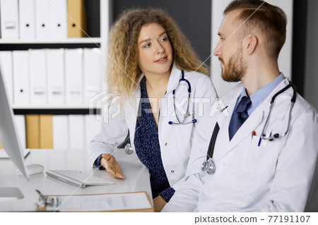 Male doctor withcolleague discussing current disease therapy while sitting at working place in clinic. Team work in medicine 77191107