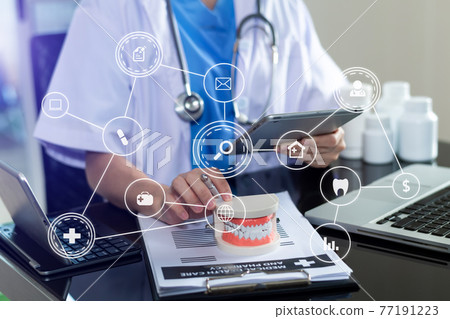 Concentrated dentist sitting at table with jaw samples tooth model and working Concentrated dentist sitting at table with jaw samples tooth model and working 77191223