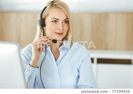 Blonde business woman sitting and communicated by headset in call center office. Concept of telesales business or home office occupation Blonde business woman sitting and communicated by headset in call center office. Concept of telesales business or home office occupation 77194936