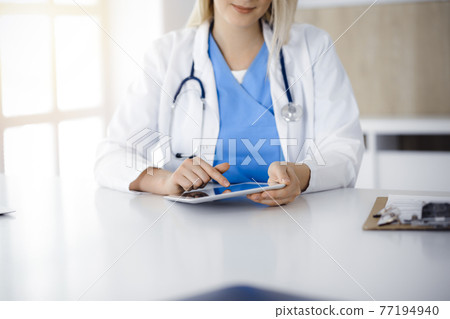 Unknown woman-doctor sitting in sunny clinic and using tablet pc, close-up. Data and best service in medicine 77194940