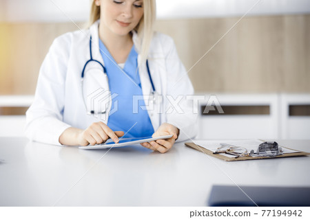 Unknown woman-doctor sitting in sunny clinic and using tablet pc, close-up. Data and best service in medicine 77194942