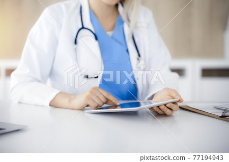 Unknown woman-doctor sitting in sunny clinic and using tablet pc, close-up. Data and best service in medicine 77194943