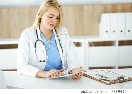 Woman-doctor standing in hospital or clinic and using tablet pc. Data and best service in medicine and healthcare Woman-doctor standing in hospital or clinic and using tablet pc. Data and best service in medicine and healthcare 77194944