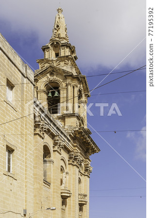 Belltower of Saint Publius Parish Church also known as the Floriana Parish Church on clear blue sky background. Ancient building with statues and architectural columns and decorations. 77195392