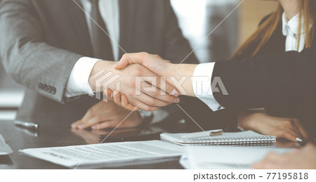 Unknown businessman shaking hands with his colleague or partner above the glass desk in modern office, close-up. Business people group at meeting 77195818