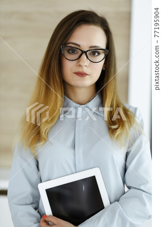 Business woman headshot at workplace in modern office. Unknown businesswoman standing straight with tablet computer. Young accountant or secretary looks good 77195904