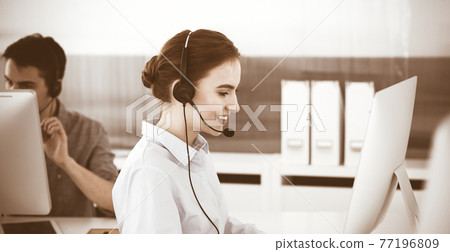 Young woman using headset and computer while talking with customers online. Group of Call center operators at work. Business concept Young woman using headset and computer while talking with customers online. Group of Call center operators at work. Business concept 77196809