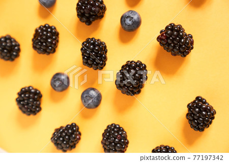 Blackberries and blueberries on a yellow background Blackberries and blueberries on a yellow background 77197342