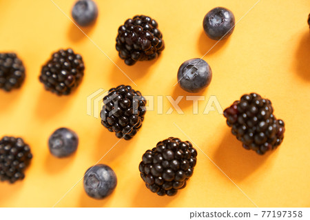 Blackberries and blueberries on a yellow background 77197358
