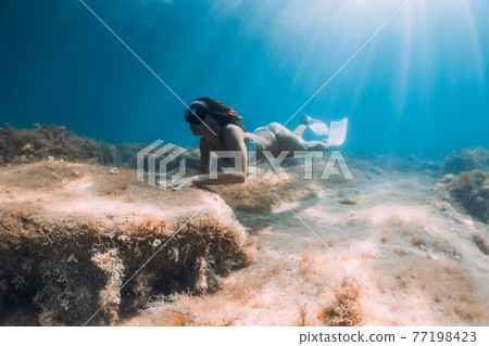 Freediver woman glides on deep sea. Free diver with fins posing underwater in blue ocean Freediver woman glides on deep sea. Free diver with fins posing underwater in blue ocean 77198423