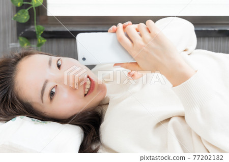 一個女人躺在床上,手裡拿著智能手機 一個女人躺在床上,手裡拿著智能手機 77202182