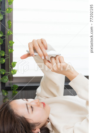A woman lying on the bed and holding a smartphone A woman lying on the bed and holding a smartphone 77202195
