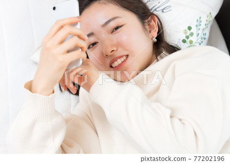一個女人躺在床上,手裡拿著智能手機 一個女人躺在床上,手裡拿著智能手機 77202196