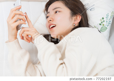 一個女人躺在床上,手裡拿著智能手機 一個女人躺在床上,手裡拿著智能手機 77202197