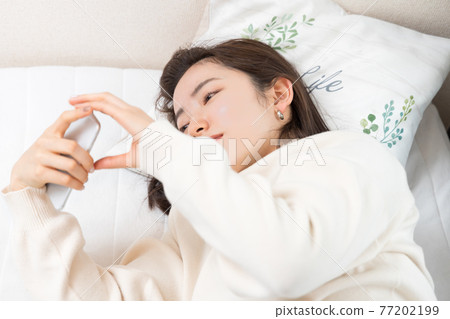 A woman lying on the bed and holding a smartphone A woman lying on the bed and holding a smartphone 77202199