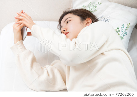 A woman lying on the bed and holding a smartphone A woman lying on the bed and holding a smartphone 77202200