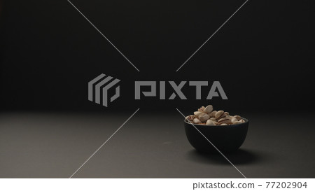 salted large pistachios in black bowl on black paper background 77202904