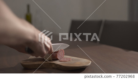 man slicing salame on olive wood board on walnut table man slicing salame on olive wood board on walnut table 77202968