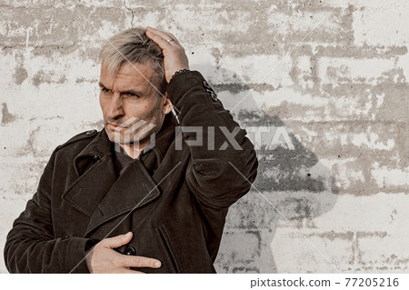 Middle aged blonde man in trendy clothes is posing in front of a white brick wall. Male fashion photoshoot. Men's mental health. Emotions. Front view, copy space. Middle aged blonde man in trendy clothes is posing in front of a white brick wall. Male fashion photoshoot. Men's mental health. Emotions. Front view, copy space. 77205216