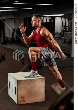 Sexy muscular men using the platform for his legs on a dark colorful background of gym. 77205684