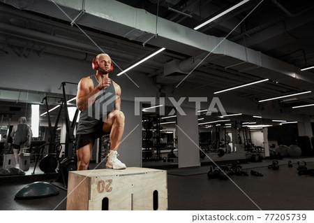 Sexy muscular men using the platform for his legs on a dark colorful background of gym. Sexy muscular men using the platform for his legs on a dark colorful background of gym. 77205739