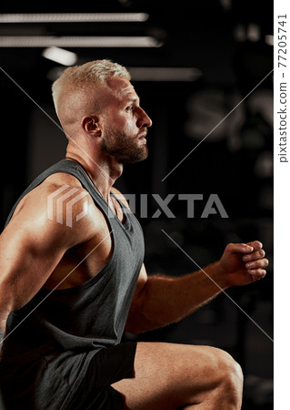 Sexy muscular men using the platform for his legs on a dark colorful background of gym. Sexy muscular men using the platform for his legs on a dark colorful background of gym. 77205741