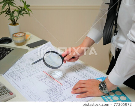 A businessman checking a blueprint using a magnifying glass 77205972